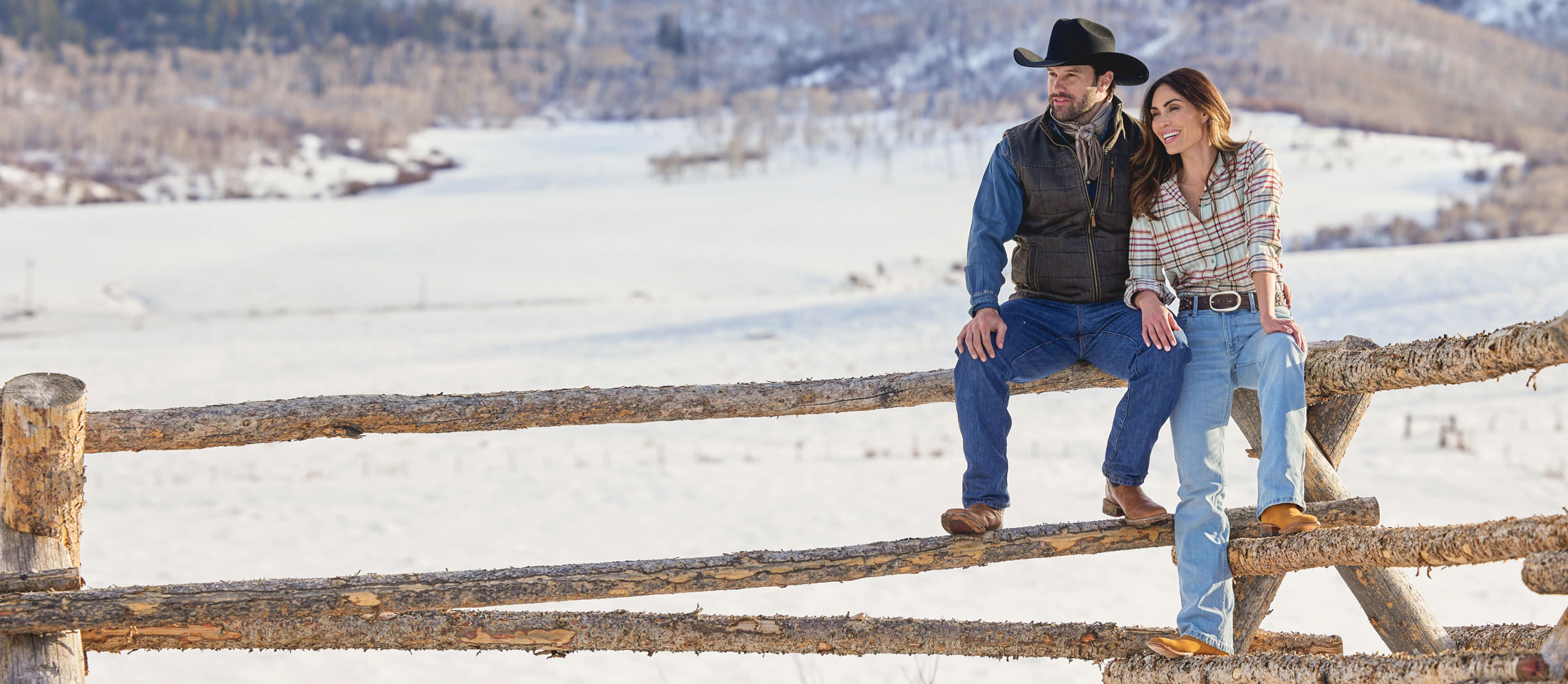 A man and a woman wearing Justin Western boots sitting on a fence made of logs.